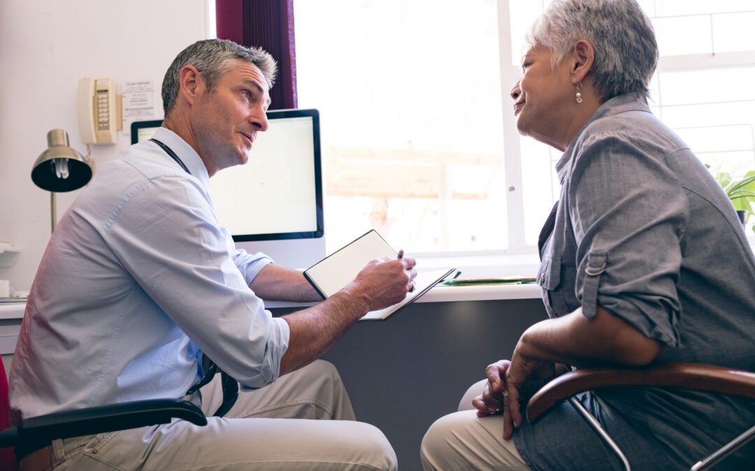 Side view of male Caucasian doctor prescribing medicine to senior African American woman in clinic at retirement home